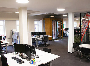 Blickwinkel des rechten Bürobereiches auf den Eingangsbereich. Eingerichtet mit Arbeitsgruppentischen und Raumtrennerschränken.