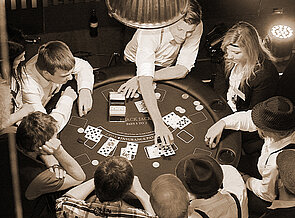 Runder Black Jack Tisch mit begeisterten Spielern außen rum. Gekleidet im zwanziger Jahre Style