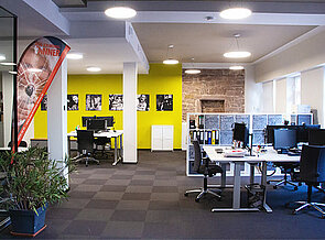 Der rechte Bereich des Büros, mit Arbeitsgruppentischen, Räumtrenner Schränken und heller Decken-Beleuchtung.