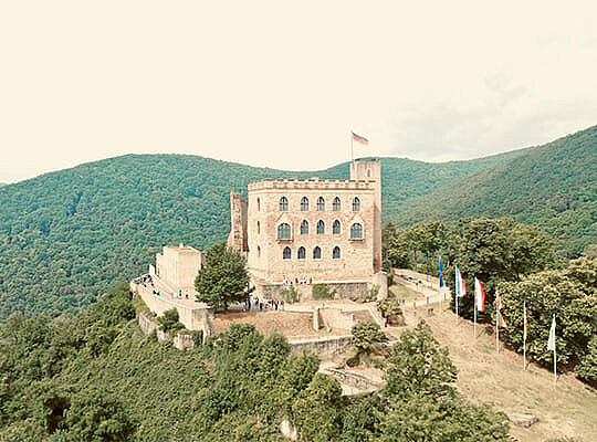 Uriges Ambiente beim Krimidinner im Hambacher Schloss 1832 Vogelperspektive auf das schöne Schlossgebäude mit bewaldeten Bergen im Hintergrund.