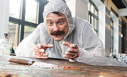 Fokussierter Blick auf ein Blutverschmierten Messers, welches auf einem Holztisch Liegt. Im Hintergrund Stehen leere Schnapsflaschen herum. Neben dem Messer liegt eine Zip Tüte.