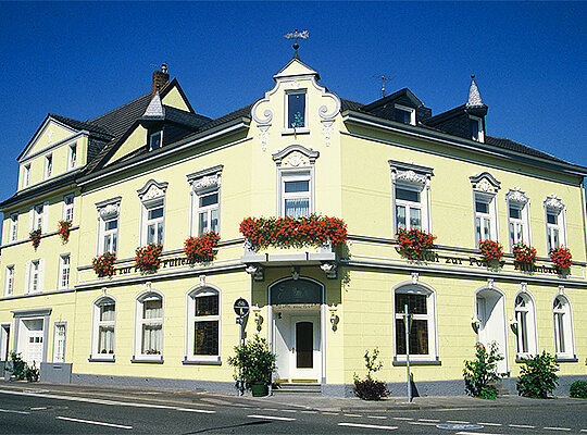 Krimidinner Bonn im Hotel Restaurant zur Post Frontalsicht auf gelbes Gebäude bei blauem Himmel dekoriert mit Blumen