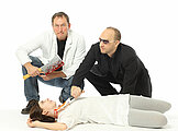 Eine Frau liegt am Boden, offensichtlich tod, während sich 2 Männer über sie beugen