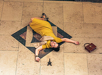 Frau im gelben Kleid liegt erschlagen im Museum auf dem Boden