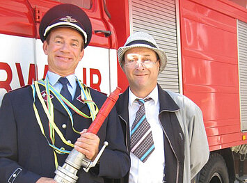 Zwei Männer mit Schlauch vor Feuerwehrauto- Krimidinner "Der Feuerwehrball"