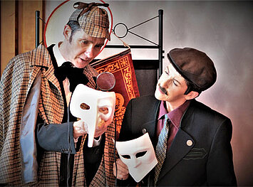 Zwei Schauspieler mit jeweils einer weißen Maske in der Hand