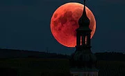Leuchtend roter Mond am Nachthimmel, etwas verdeckt durch einen Kirchturm