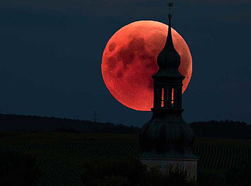 Leuchtend roter Mond am Nachthimmel, etwas verdeckt durch einen Kirchturm
