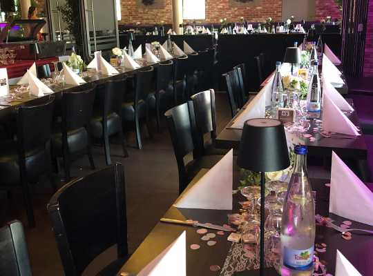 Viel Spaß beim Krimidinner im Restaurant Merlin wünscht Das Kriminal Dinner! Große, lange Tafeln in dunklem Holz mit weißen Servietten gedeckt