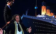 Zwei der damaligen Zeit gemäß gekleidete Künstler stehen vor der gigantischen Titanic.