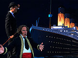 Zwei der damaligen Zeit gemäß gekleidete Künstler stehen vor der gigantischen Titanic.