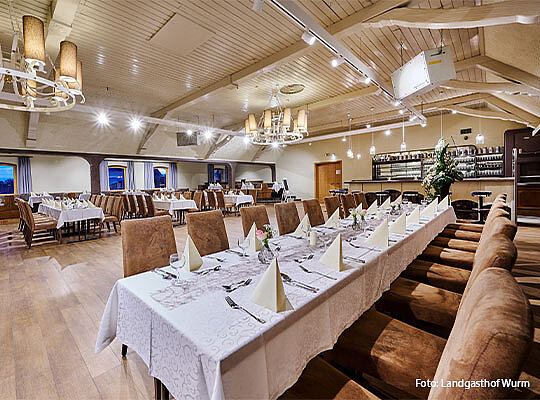 Innenansicht des Gasthauses auf eine Lange Tischtafel, an welcher Stühle stehen.