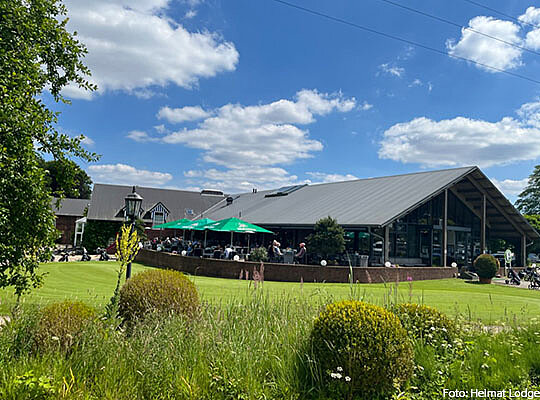 Außenansicht der HeimatLODGE, davor eine grüne Wiese und einem blauen Himmel mit Wolken