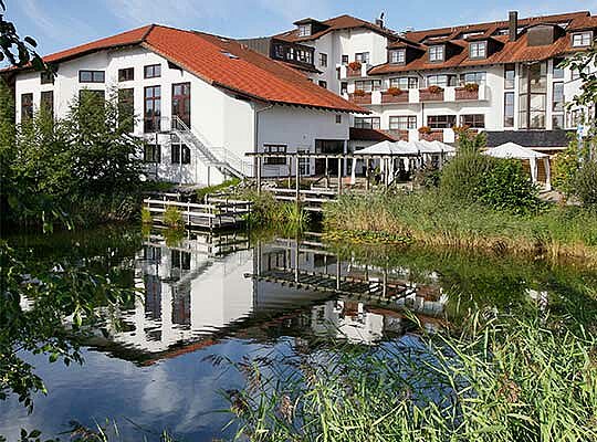 Außenansicht des Alpen Resort mit einem See vor der Haustüre beim Krimidinner