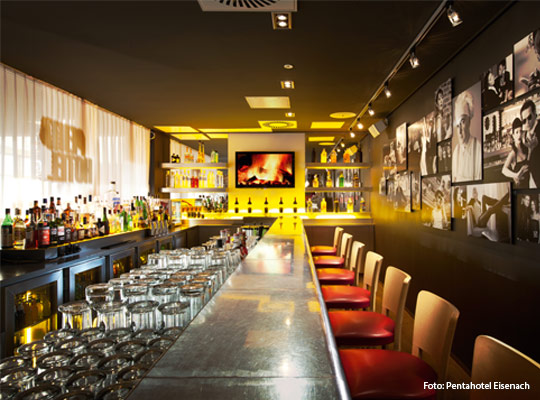 Lange Barzeile mit roten Barhockern in gedämpfter Lichtstimmung