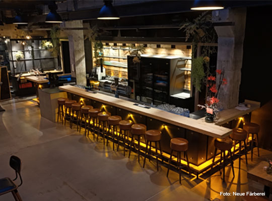 Blick auf die schön beleuchtete Bar mit vielen Barhockern