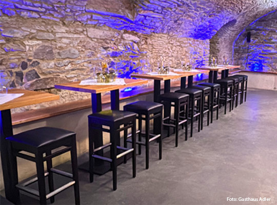 schön beleuchteter Gewölbekeller mit Stehtischen und Barhockern