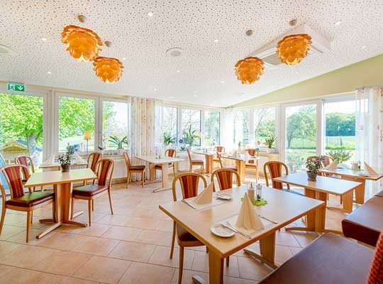 Veranstaltungssaal modern eingerichtet mit Tischen aus hellem Holz und orangenen Deckenleuchten