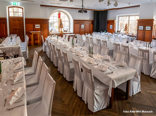 festlich eingedeckter Speisesaal mit langen Tafeln und Holztäfelung an der Wand