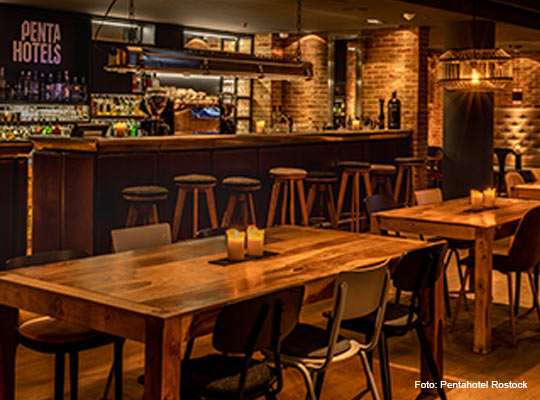 Lange Bar mit großen Holztischen davor