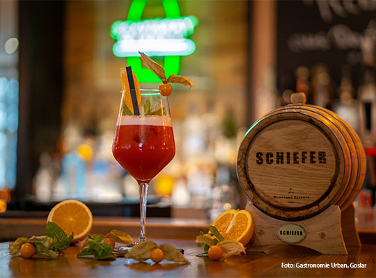 Ein roter Cocktail steht neben einem kleinen Fass aus Holz