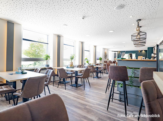 Großer Innenraum mit Bar-Stühlen welche im Raum verteilt an Tischen stehen. Zu sehen ist außerdem eine Theke