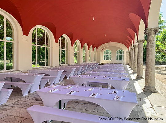 Großer, heller Saal mit runden Tischen und roten Akzenten