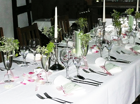 Wunderschön angerichtete lange Tafel, mit weißer Tischdecke und grünen Blumen.