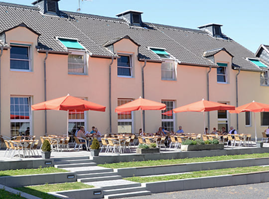 Außenansicht der Klosterstube mit großen Sonnenschirmen auf leicht erhöht liegender Terrasse in strahlendem Sonnenschein