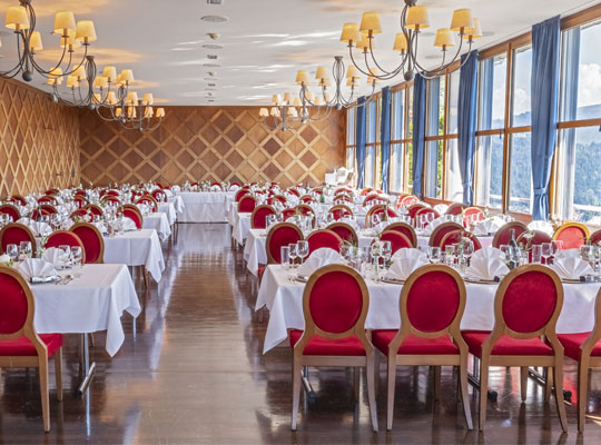 Festlicher Speißesaal im Burgrestaurant. Goldene Kronleuchter und rote Stühle. An den großen Fenstern hängen blaue Vorhänge