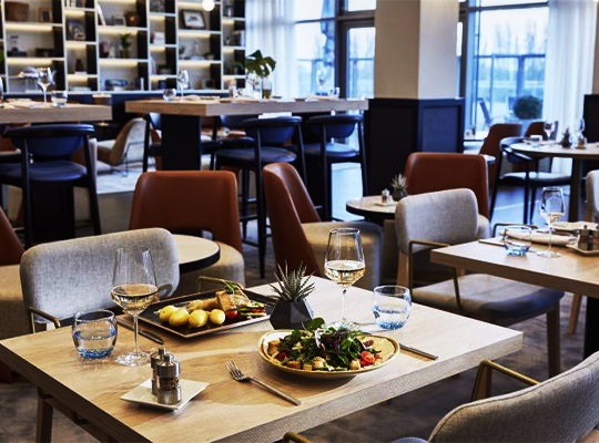 Heller Restaurantbereich, ausgestattet mit bequemen Stühlen und modernen Esstischen. Der vorderste Tisch ist gedeckt mit einladenden Gerichten.