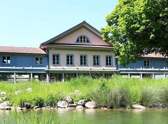 Blick vom Dorfbach Oberburg auf das blau gestrichene Schützenhaus.