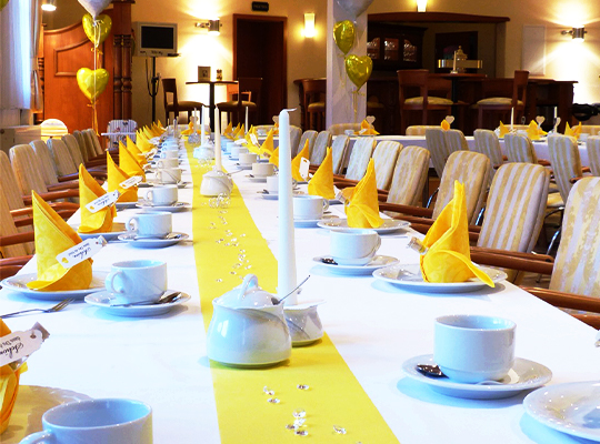 Festlich angerichtete lange Tafel mit goldenen Servietten und gold-weiß gepolsterten Stühlen.