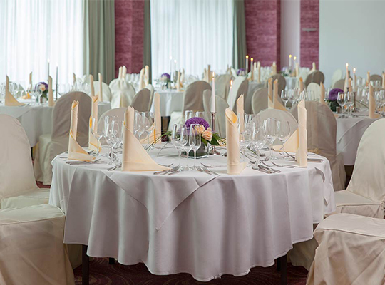 Feinst dekorierter und angerichtete Tische mit weißen Tischdecken, beigen schön gefalteten Servietten und weißen Stuhl-Hussen.