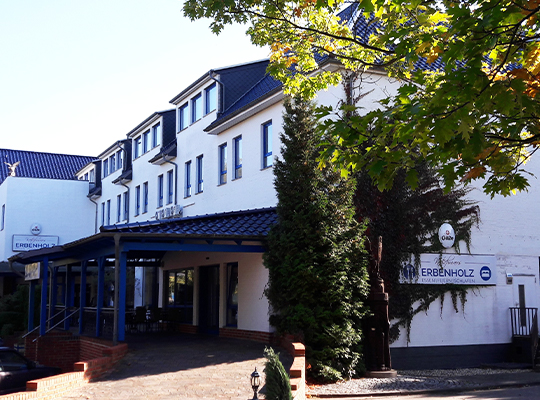 Blick auf den Eingangs- und Terrassenbereich des modernen, weiß gestrichenen Restaurants. Im Vordergrund ist eine schön mit Backsteinen gepflasterte Rampe zum Außenbereich zu sehen. 