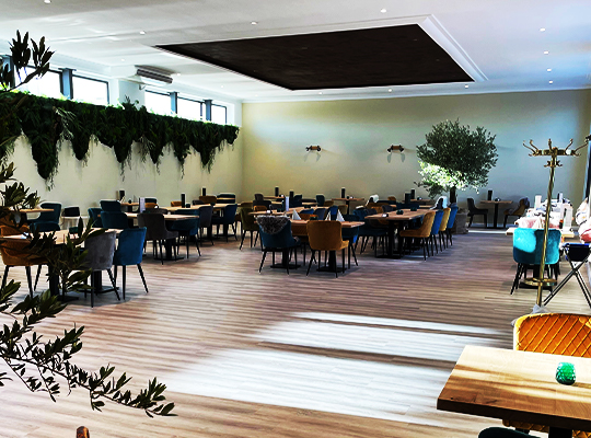 Großer Festsaal mit einzelnen Tischgruppen gefüllt und ausgewählten grünen Pflanzen/Bäumen