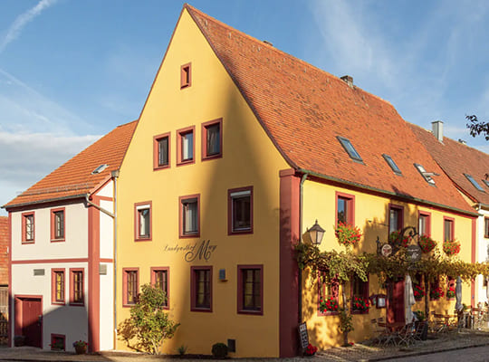 Straßenansicht auf das gelbe, mit Blumen geschmücktes Landgasthof-Gebäude.