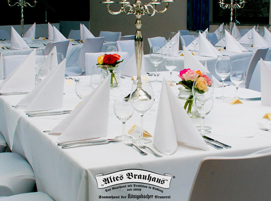 Weiß gedeckte Tische mit Rosen und edlem Gedeck, Kerzenleuchter thronen in der Mitte des Tisches