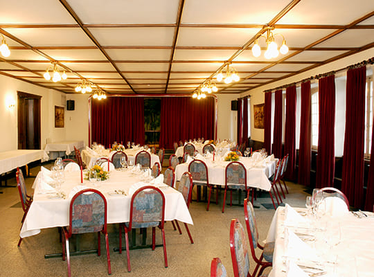 Großer Speisesaal mit bunt gepolsterten und rot umrahmten Stühlen, weißen Tischdecken und roten Vorhängen. 