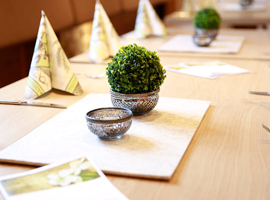 Schlicht eingedeckter Holztisch mit kleinen grünen Gestecken und schön drapierten Servietten
