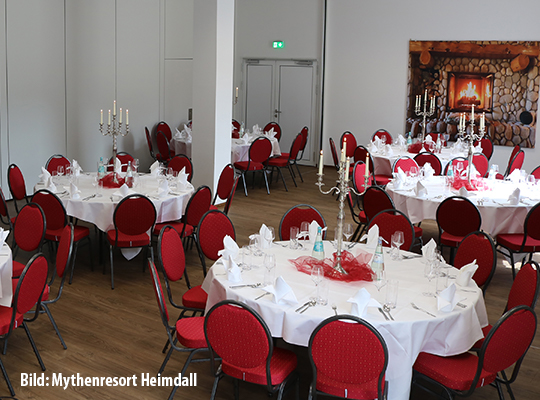 Schön dekorierte Tischgedecke mit bequemen roten Stühlen in einem weißen Speiselsaal mit einem Kaminofen-Bild an der Wand