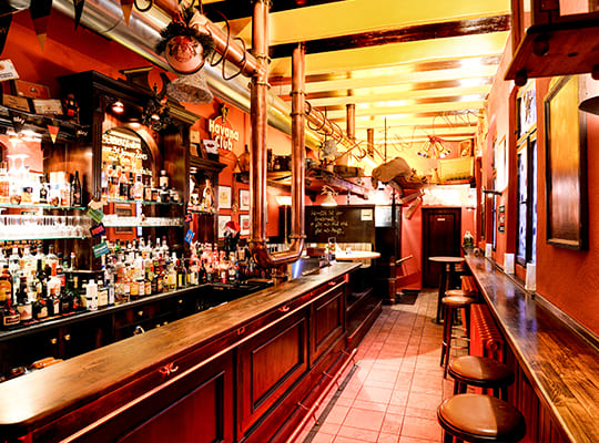Urig eingerichtete Lange Bar-Theke mit alten Messingrohren die von der Decke hängen und Barhockern als Sitzgelegenheit.