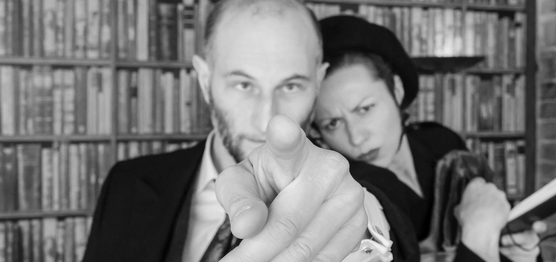 Krimidinner Firmenveranstaltungen buchen Mann zeigt mit dem Finger in die Kamera während sich eine Frau von rechts an ihn lehnt