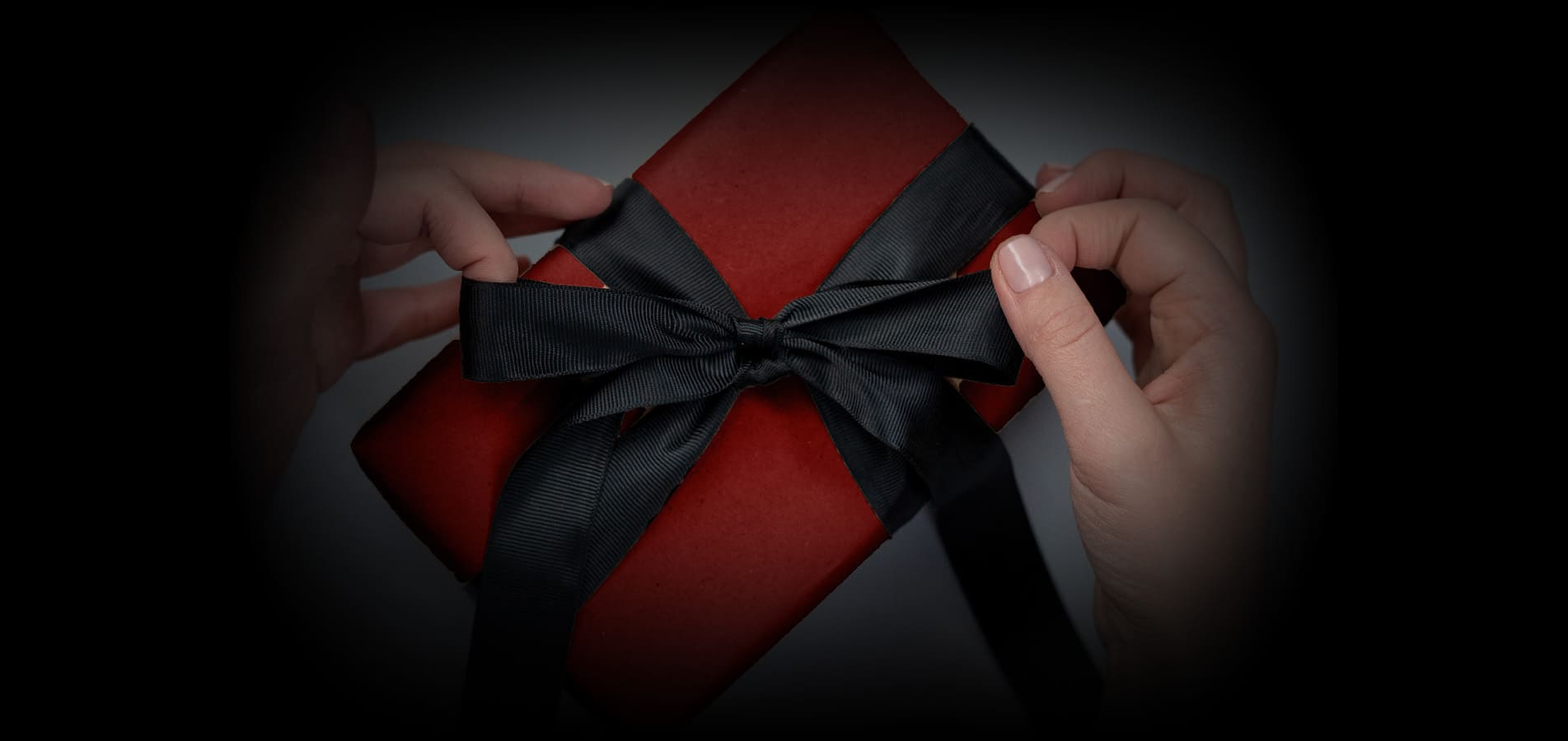 Zwei Hände öffnen die Schlaufen eines Geschenks