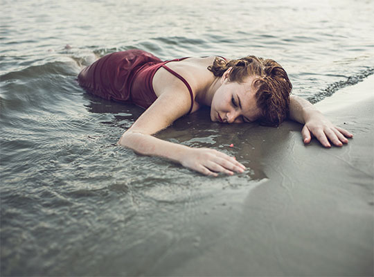 Eine Frau in einem roten Kleid liegt ohnmächtig im Meer