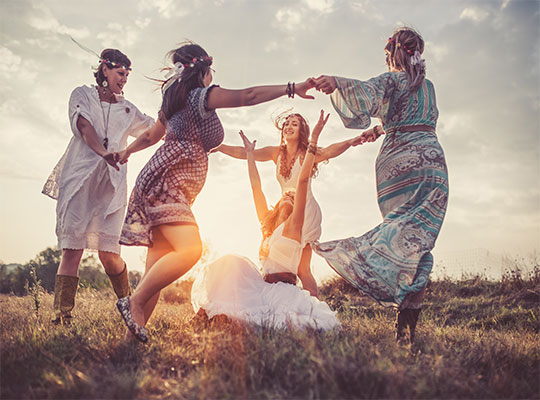 Vier Hippies tanzen um ein Hippie Mädchen das auf den Boden sitzt 