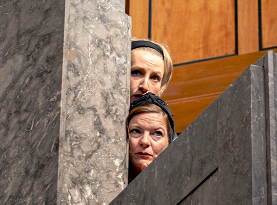 Zwei Frauen spicken durch die Mauern im Museum und beobachten etwas