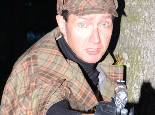 Sherlock Holmes steht versteckt an einem Baum mit einer Pistole - spannendes Krimidinner im Schwabenland