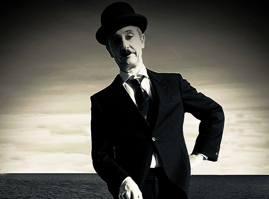Ein wie Charlie Chaplin gekleideter und geschminkter Künstler auf einem schwarz-weiß Foto.