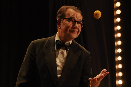 Mann in Anzug der mit einer Hand einen kleinen Ball in die Luft wirft
